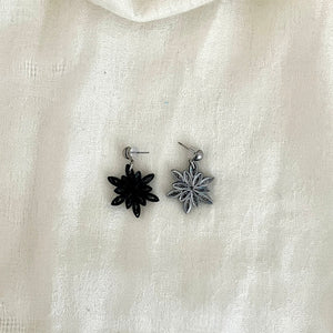 Paper quilled Snowflake earrings in black with silver edge color. One earring is showing the front side (silver color) and the other earring is showing the back side (black color).