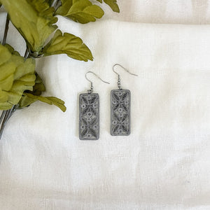 Handmade paper quilled earrings in grey color in a thin rectangle shape with tile like patterns.